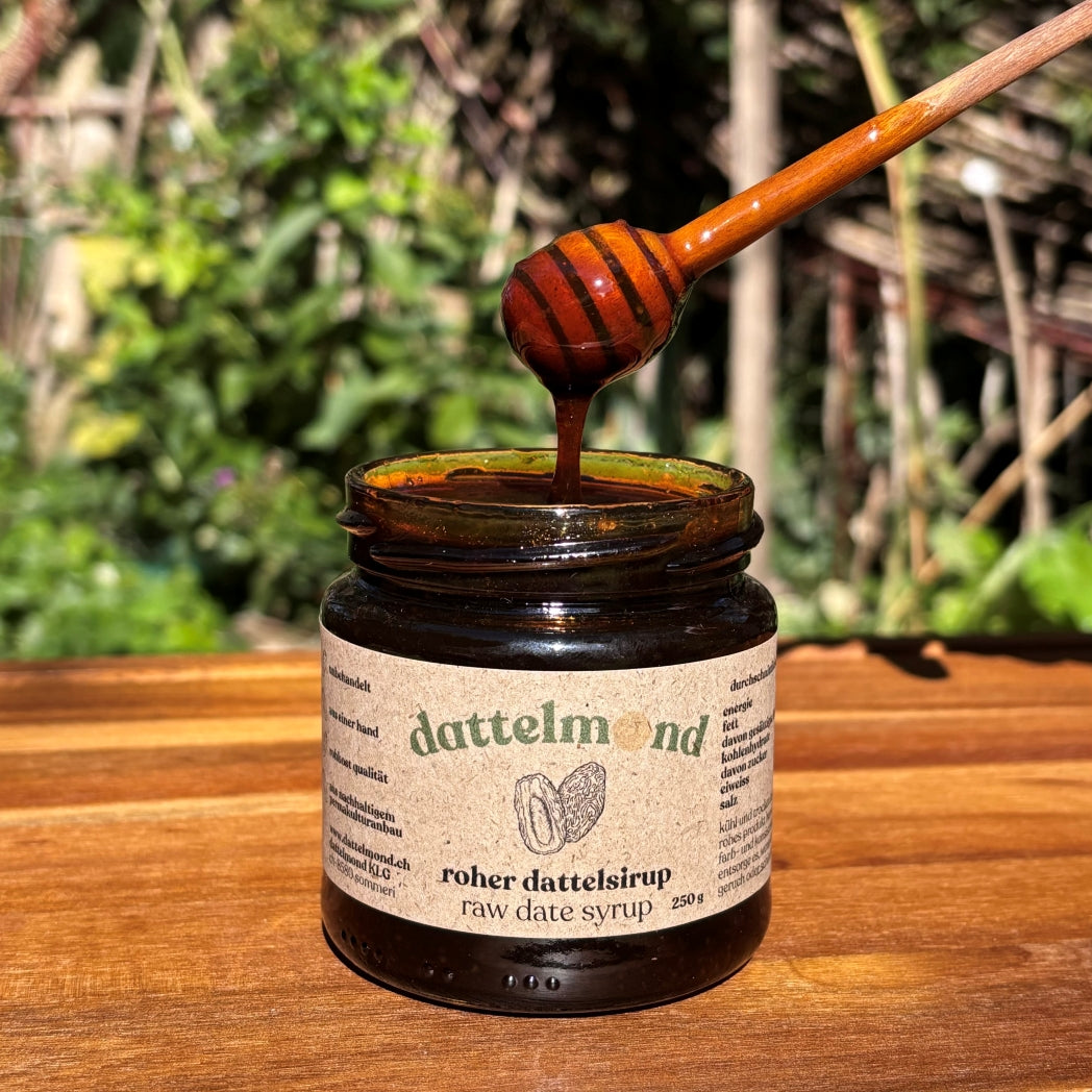 Glas Dattelmond roher Dattelsirup mit einem Honiglöffel auf einer Holzoberfläche.