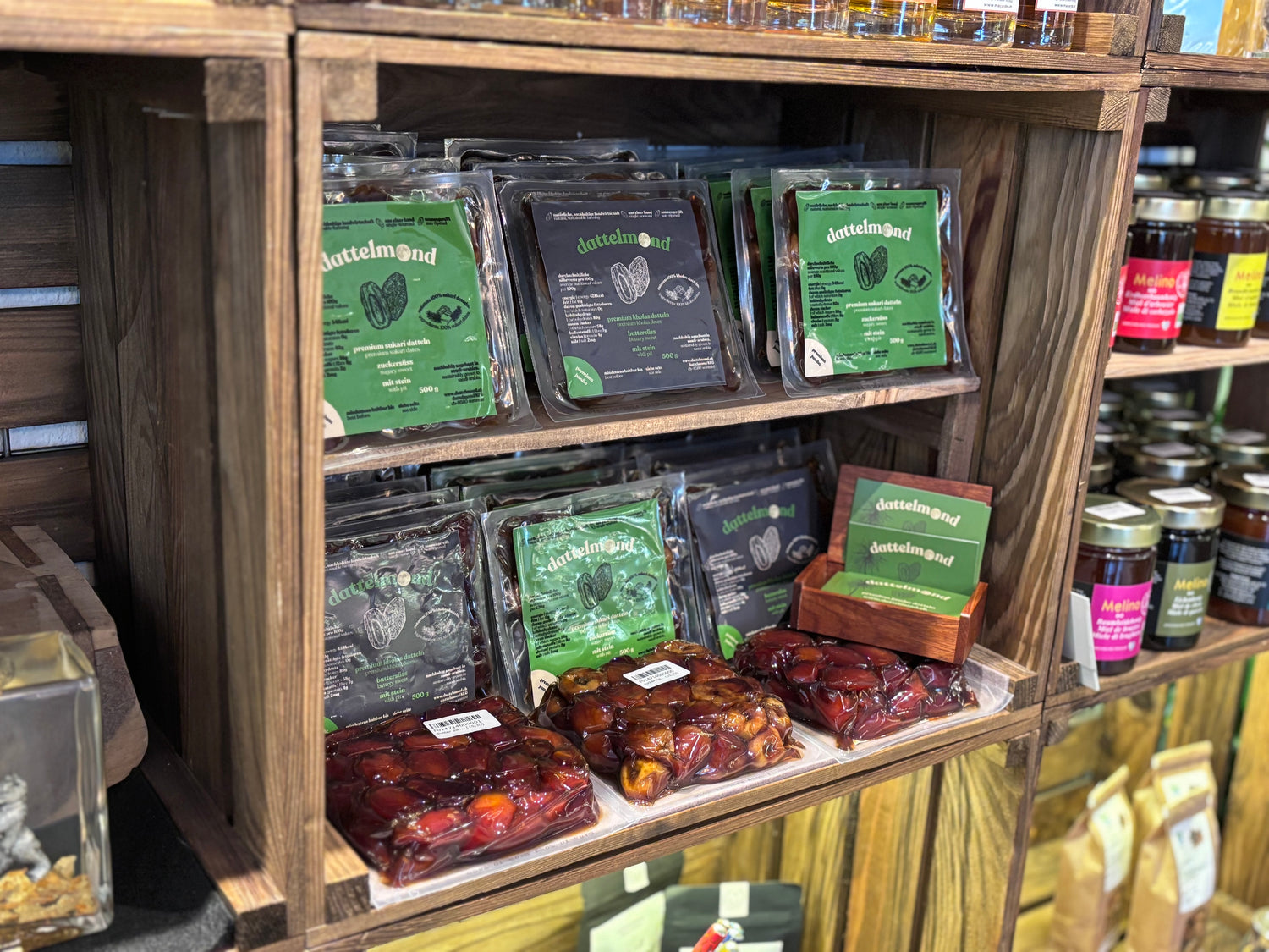 Dattelmond Produkte auf einem Holzregal im s’Fachl St. Gallen, neben einer Holzbox mit ihren Visitenkarten.