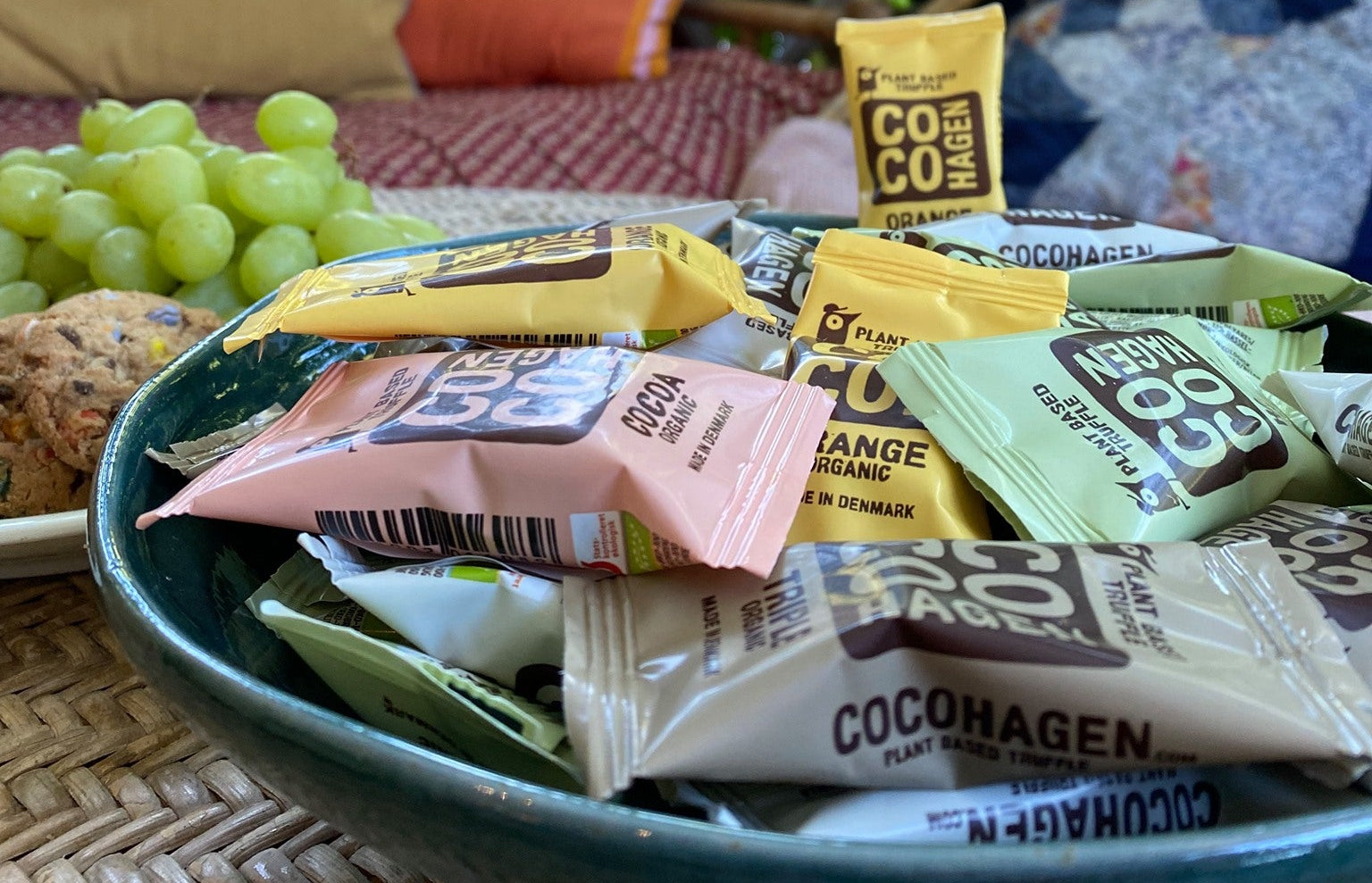 Assorted Cocogreen packets on a plate with grapes and cookies, outdoor setting