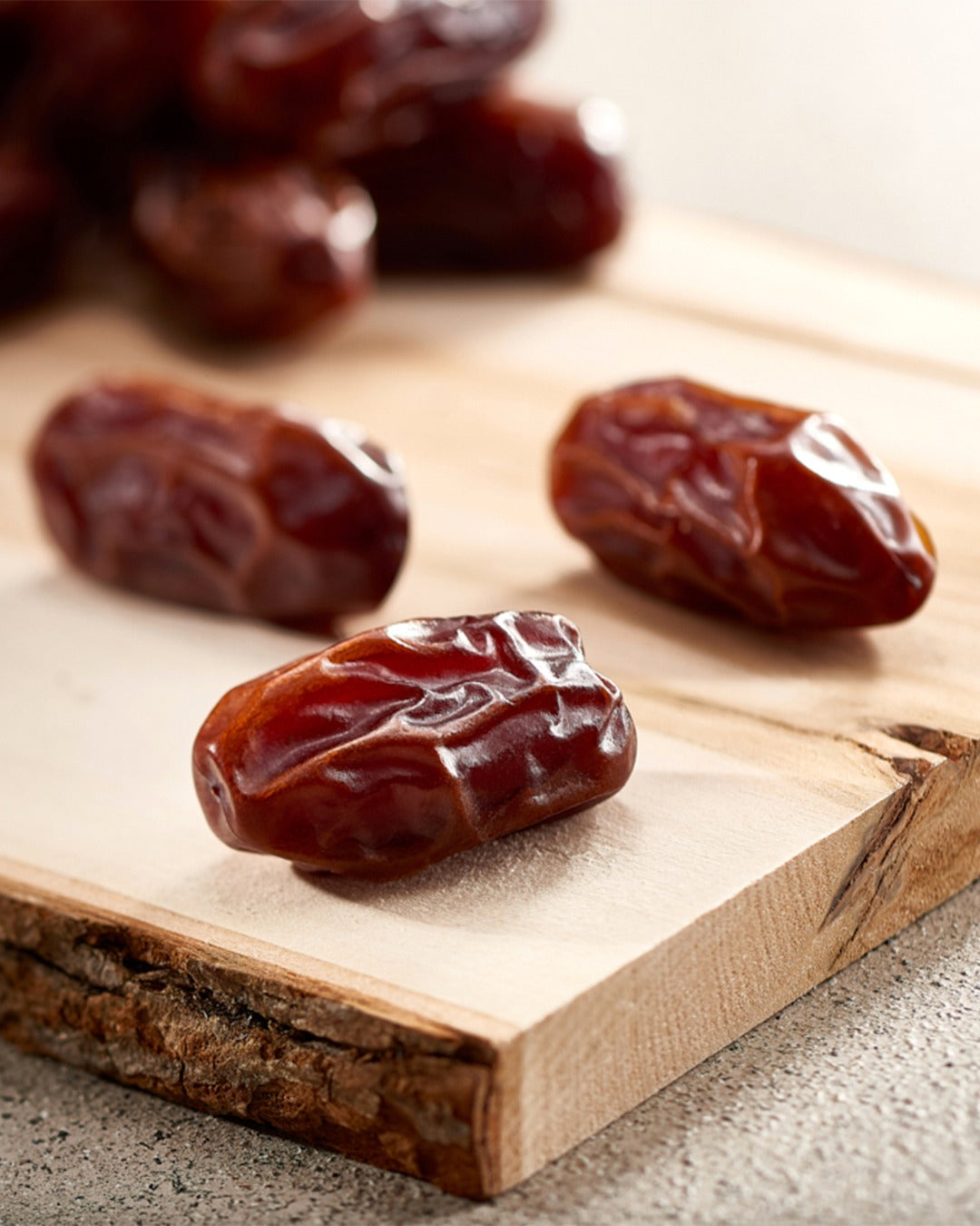 Three Khidri dates on a wooden cutting board with a blurred background