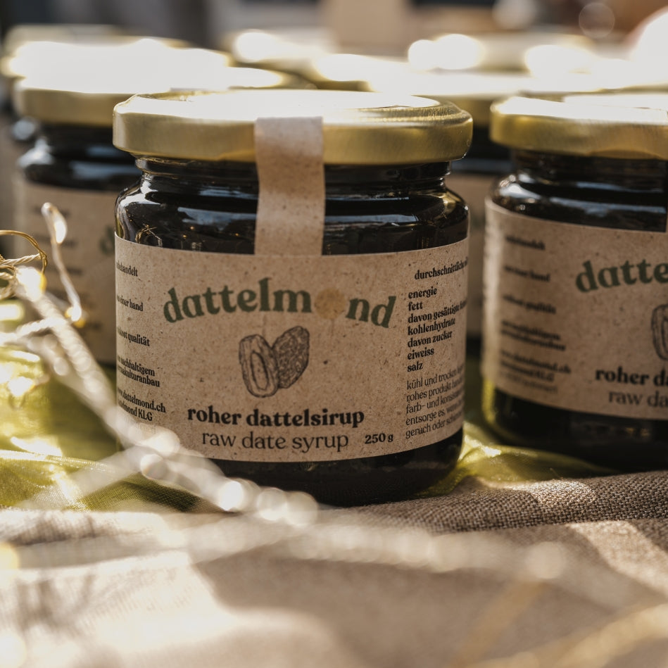 Jars of dattelmond raw date syrup on a textured surface with blurred lights in the background