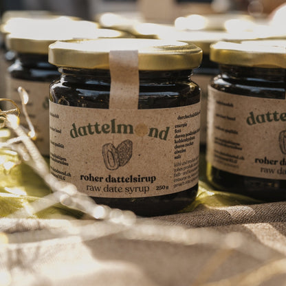 Jars of dattelmond raw date syrup on a textured surface with blurred lights in the background