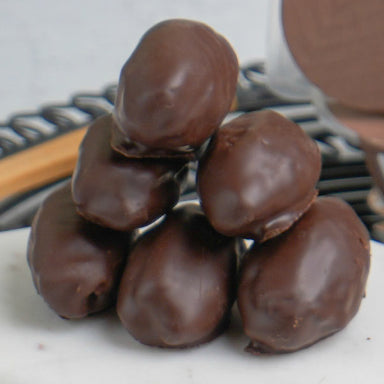 Chocolate-covered dates on a plate with a wooden spoon and cocoa powder in the background.